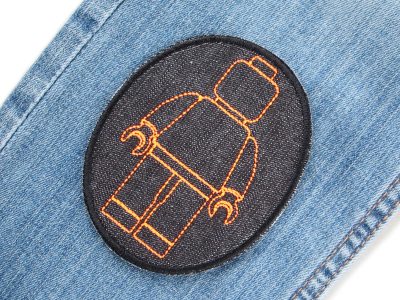Neonorange Bausteinmännchen-Knieflicken auf Kinderhose aufgebügelt, schwarzer Jeansstoff 8 x 10 cm mit neonorangenen Spielfiguren, Bügelflicken Kinderhosen reparieren Piratenbande Berlin