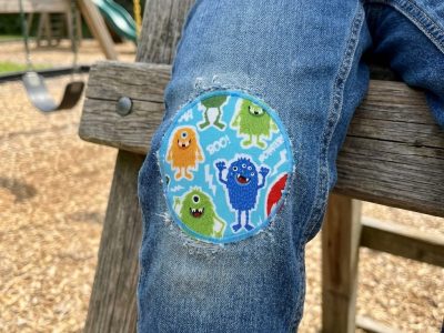 runder Monster Hosenflicken zum aufbügeln aus Baumwollstoff auf einer Kinderhose - Monster Hosenflicken hellblau Ø 8 cm auf Kinderhose aufgebügelt, bunter Baumwollstoff mit fröhlichen Monstern, Knieflicken handmade Berlin