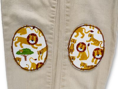 Löwen-und-Tiger-Knieflicken auf Kinderhose aufgebügelt, heller Baumwollstoff 8 x 10 cm mit bunten Löwen und Tigern Safari-Allover, Bügelflicken Kinderhosen reparieren Piratenbande Berlin