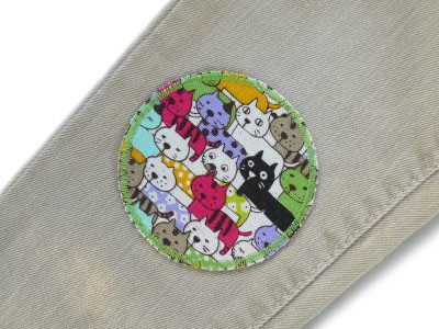 Bunter Katzen-Bügelflicken auf Kinderhose aufgebügelt, Baumwollcanvas Ø 7 cm mit buntem Katzen-Allover, Hosenflicken Kinder reparieren Piratenbande Berlin