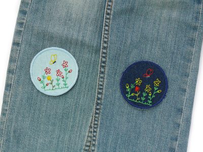 Patches zum aufbügeln mit Blumen als Knieflicken auf einer Kinderhose – Blumenwiesen-Bügelflicken Ø 7 cm auf Kinderhose aufgebügelt, Jeans hellblau mit gestickten Blumen und Schmetterling, Knieflicken handmade Berlin Piratenbande