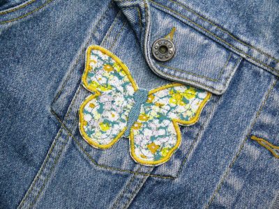 Schmetterling Bügelpatch gelb auf Jacke aufgebügelt, gelb-weiß geblümter Baumwollstoff 9,5 x 7 cm mit bunter Stickerei, Schmetterling-Aufnäher handmade Berlin Piratenbande