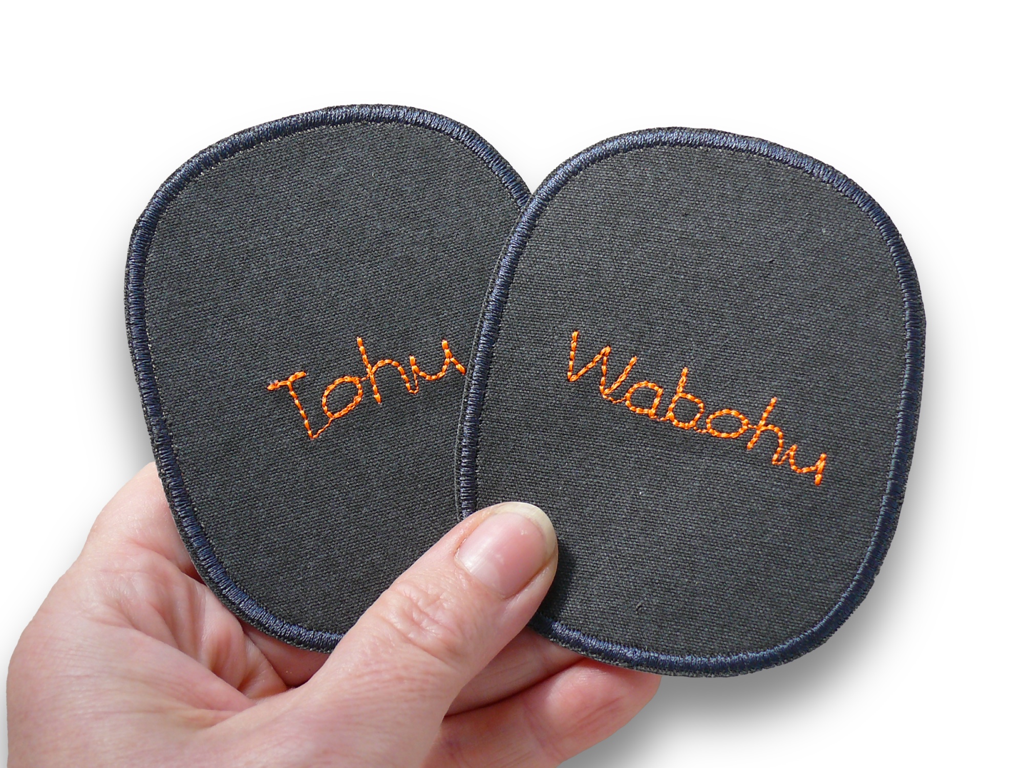 Nahaufnahme Knieflicken Tohu Wabohu, 8 x 10 cm dunkelgrauer Canvas mit neonoranger Schrift, Statement-Bügelflicken handmade Berlin Piratenbande