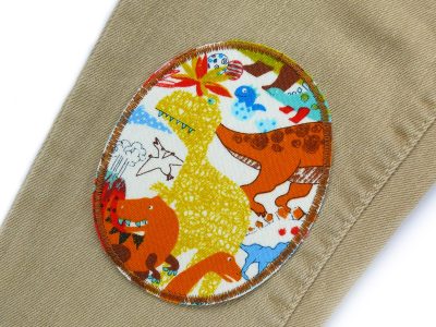Dino-Knieflicken auf Kinderhose aufgebügelt, heller Baumwollstoff 8 x 10 cm mit bunten Dinosauriern, Bügelflicken Kinderhosen reparieren Piratenbande Berlin
