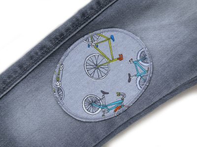 Grauer Fahrrad-Knieflicken auf Jeanshose aufgebügelt, Baumwollcanvas 8 x 10 cm mit buntem Fahrrad-Allover, Hosenflicken Bügelflicken für Kinderhosen handmade Berlin Piratenbande