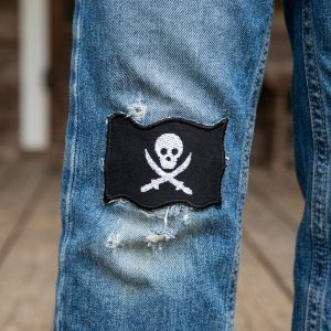 schwarzer Piratenflagge-Patch mit weißem Totenkopf auf einer Jeanshose – Jolly Roger Bügelpatch 7 x 5 cm auf Jeans aufgebügelt, handmade Berlin Piratenbande