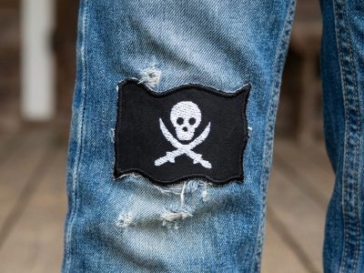 schwarzer Piratenflagge-Patch mit weißem Totenkopf auf einer Jeanshose – Jolly Roger Bügelpatch 7 x 5 cm auf Jeans aufgebügelt, handmade Berlin Piratenbande