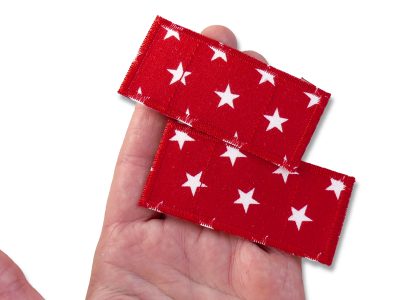 Zwei rote Stern-Hosenpflaster aus Baumwollstoff auf einer Hand, 7,5 x 3,5 cm, weiße Sterne auf Rot, Pflaster-Bügelflicken handmade Berlin Piratenbande