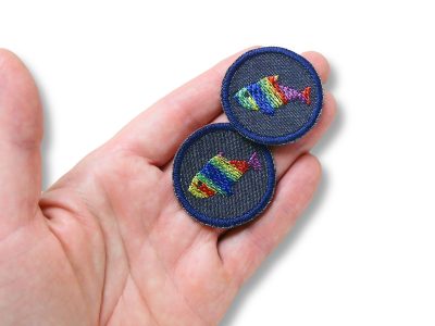 Regenbogenfisch-Bügelflicken auf Hand, dunkelblaue Mini-Jeansflicken Ø 4 cm mit buntem gesticktem Fisch in Regenbogenfarben, Aufnäher für Shirts Jacken Taschen Piratenbande Berlin