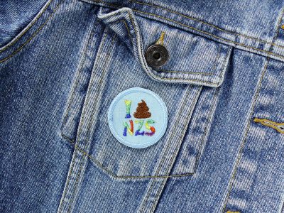 Patch zum aufbügeln I-shit-Nzs auf einer Jeansjacke, Statement Bügelflicken gegen Rechts und für Demokratie, Durchmesser 4,5 cm, gestickt in Regenbogen-Farben auf hellblauen Jeansstoff, Handmade in Berlin