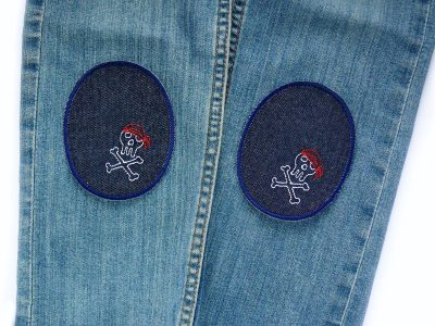 Piraten-Totenkopf-Knieflicken auf Kinderhose aufgebügelt, dunkelblauer Jeansstoff 8 x 10 cm mit bunten Totenköpfen, Hosenflicken Kinderhosen reparieren Piratenbande Berlin