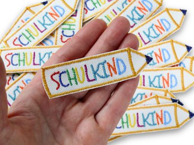 Nahaufnahme Schulkind Aufnäher, gestickter Bleistift 9 x 2,5 cm mit Regenbogen-Buchstaben auf weißem Jeans, Bügelpatch handmade Berlin