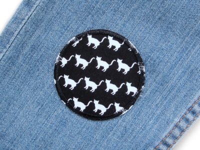 Katzen-Bügelflicken auf Kinderhose aufgebügelt, schwarzer Baumwollstoff Ø 6 cm mit weißen Katzen-Motiven, Hosenflicken Kinder Bügelflicken Piratenbande Berlin