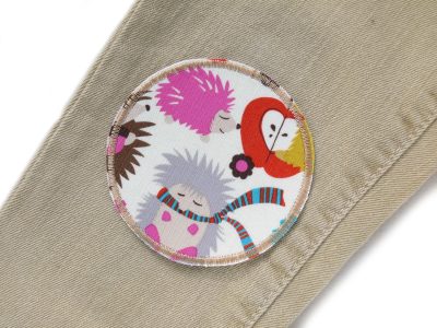 Igel Hosenflicken auf Kinderhose aufgebügelt, heller Baumwollstoff Ø 8 cm mit bunten Igel-und-Blumen-Allover-Muster, Bügelflicken handmade Berlin Piratenbande