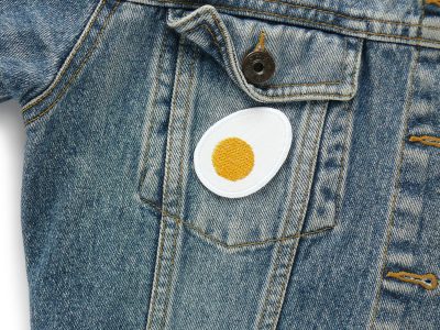 Ei Patch auf Jeansjacke aufgebügelt, weißer Baumwollstoff 5,5 x 4 cm mit gesticktem Eidotter, Bügelflicken Deko handmade Berlin Piratenbande