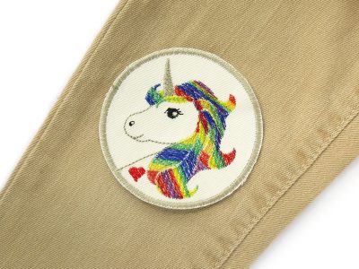 Einhorn-Patch auf Jeans aufgebügelt, cremefarbener Baumwollcanvas Ø 8 cm mit gesticktem Einhorn und bunter Regenbogen-Mähne, Bügelflicken handmade Berlin Piratenbande