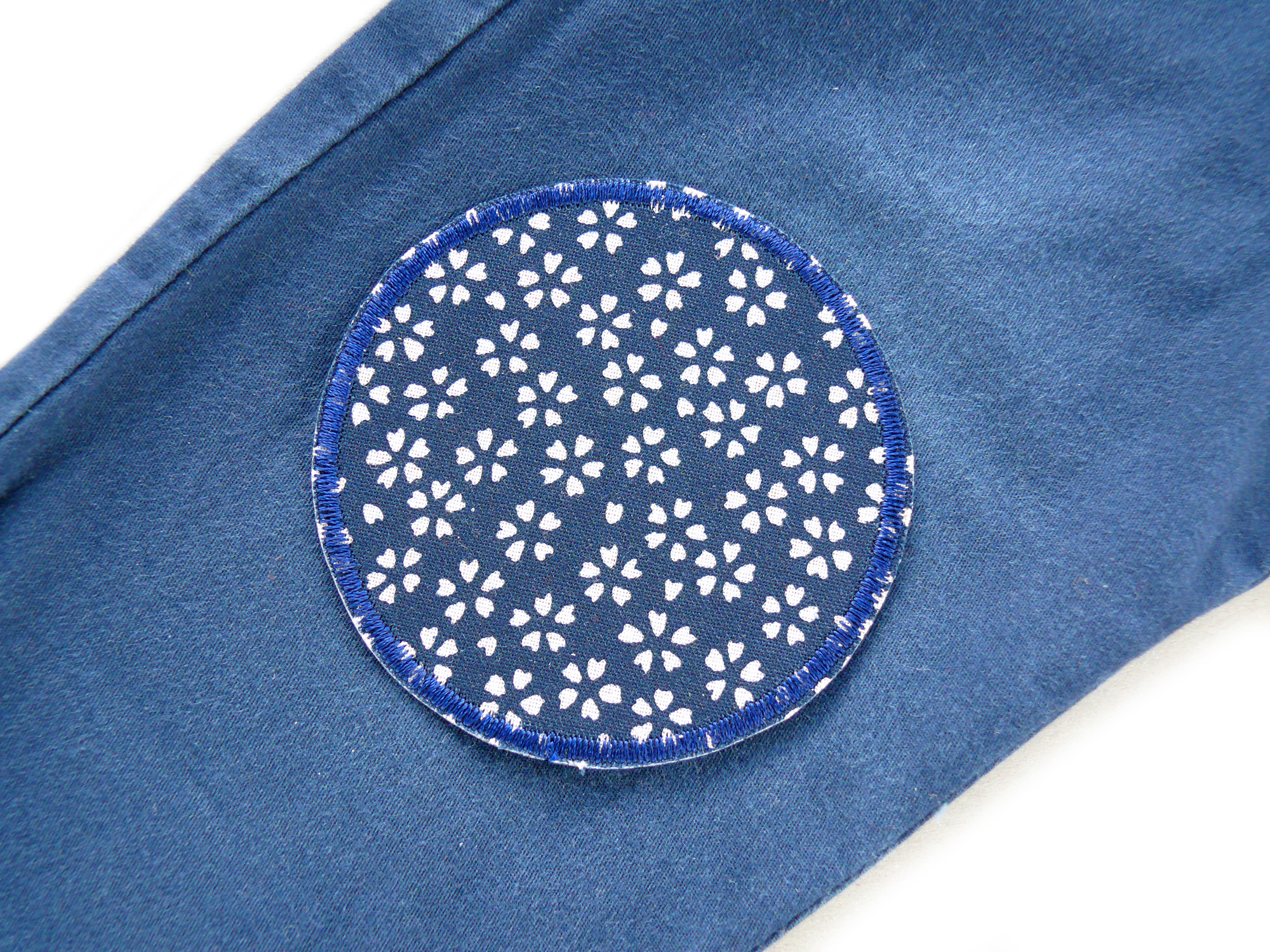 dunkelblauer Hosenflicken mit Blumen auf einem blauen Hosenbein, Blüten-Hosenflicken dunkelblau Ø 7 cm, helle japanische Blüten auf dunkelblauem Baumwollstoff, Bügelflicken handmade Berlin Piratenbande