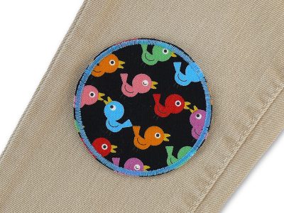 Bunte Vögelchen Bügelflicken auf Kinderhose aufgebügelt, schwarzer Baumwollcanvas Ø 7 cm mit buntem Vogel-Allover-Muster, Hosenflicken Kinderhosen reparieren Piratenbande Berlin