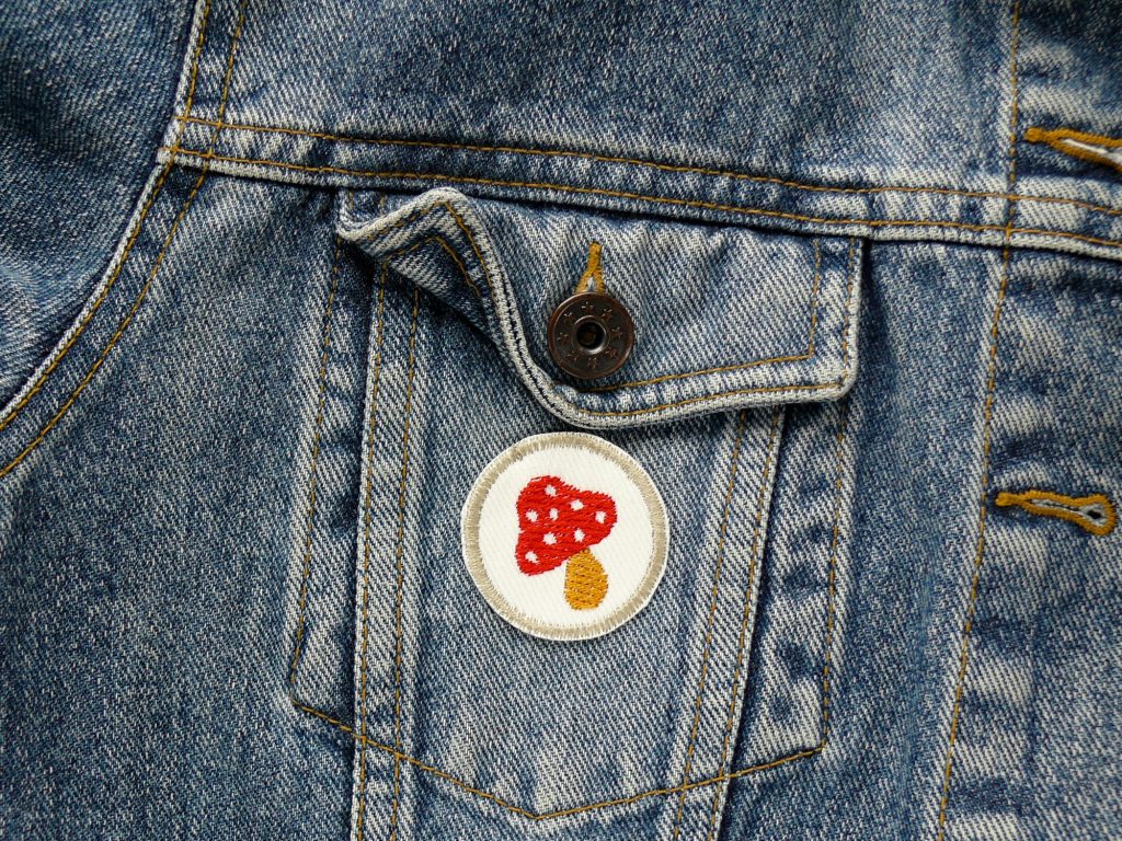 kleiner Patch mit gesticktem roten Fliegenpilz auf einer Jeansjacke, 4 cm, Handmade Berlin Piratenbande – Fliegenpilz Mini-Patch Ø 4 cm weißer Jeans mit rotem Pilz und ockerfarbenem Rand auf Jeansjacke, Bügelflicken Aufnäher handmade Berlin
