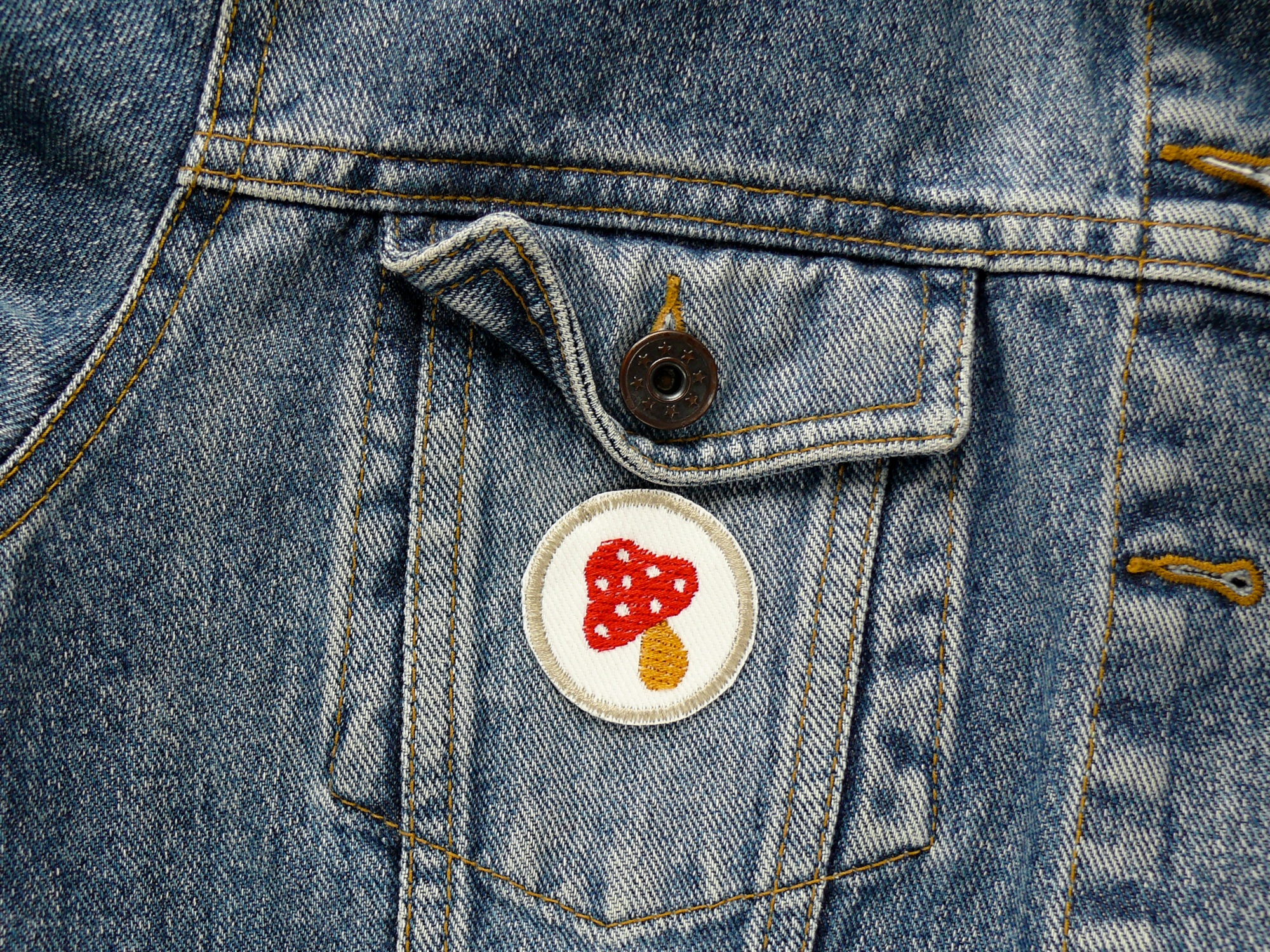 kleiner Patch mit gesticktem roten Fliegenpilz auf einer Jeansjacke, 4 cm, Handmade Berlin Piratenbande – Fliegenpilz Mini-Patch Ø 4 cm weißer Jeans mit rotem Pilz und ockerfarbenem Rand auf Jeansjacke, Bügelflicken Aufnäher handmade Berlin